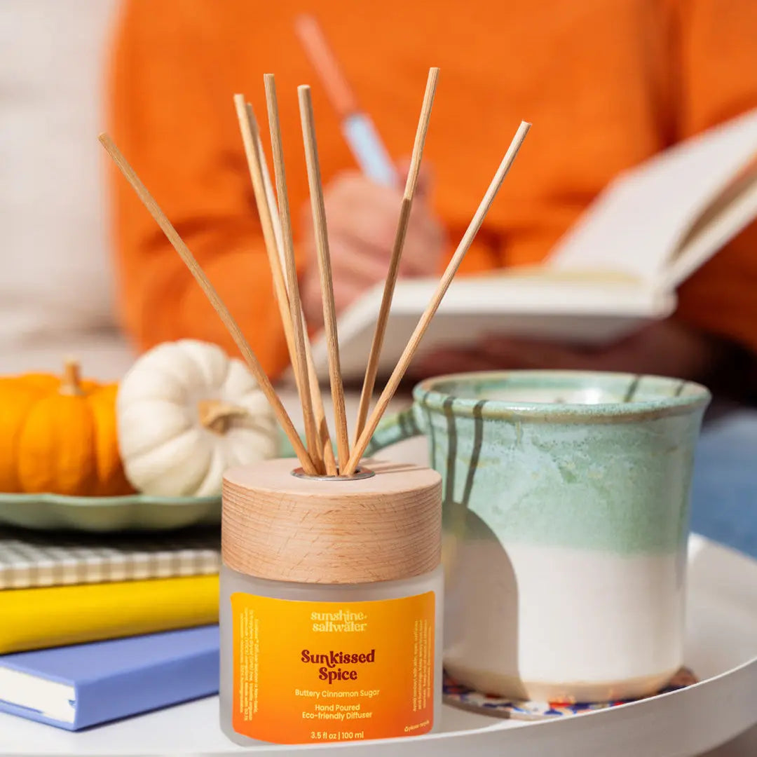 A diffuser with wooden sticks on a table, with a person in an orange sweater in the background.